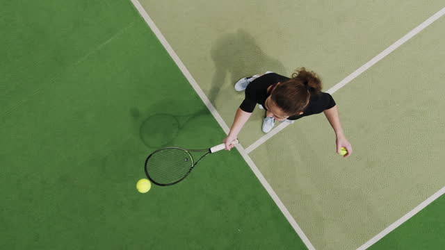 SLO MO Directly Above Shot of Young Female Tennis Player Bouncing Ball on Racket while Standing on Court in Sports Club