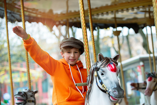 Happy boy rides on a vintage carousel horse and waves his hand. Childhood memories.