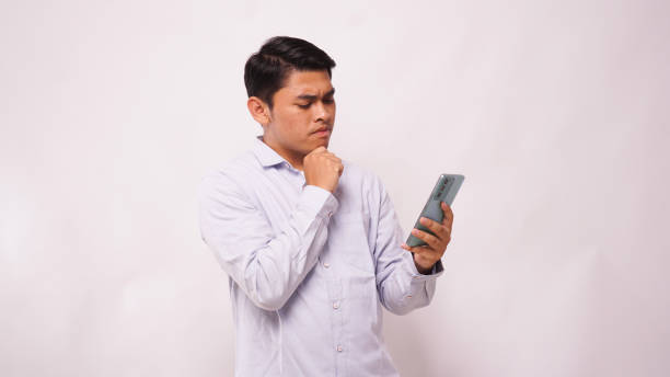 istock Adult Asian man thinking about something while holding mobile phone on studio shot 1942392468