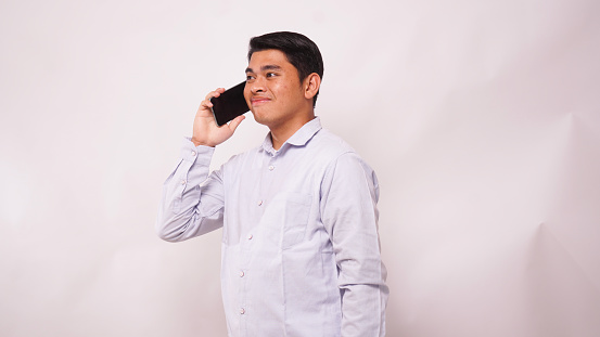 Asian man smiling at camera while answering a mobile phone call on white background
