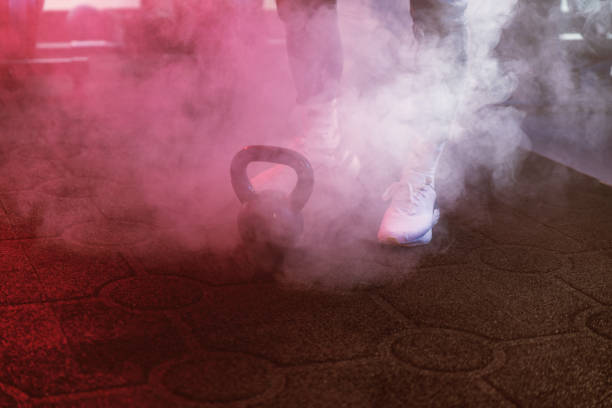 Close-up shot of an athlete's feet around a black kettlebell, set in moody blue and red lighting with a hazy atmospherex
