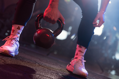 A gym session's moody essence captured in the poised feet of an athlete ready to lift a black kettlebell