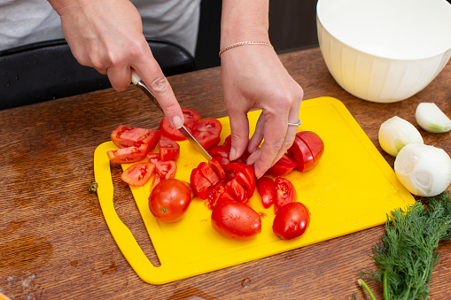 Hands cut tomatoes on a cutting board. Prepare vegetable salad.