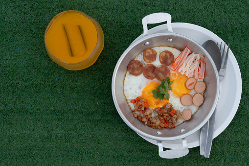 Pan Fried Eggs Topped with minced pork, hot flowers, Chinese sausage and crab sticks. Served in a galvanized plate and placed on a plate. Served with orange juice. Placed on artificial grass
