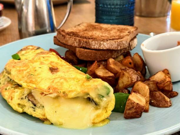 Cropped image of a young woman sits at a table and eats breakfast with omelette eggs with sausage and grilled cherry tomatoes, setting the stage for a great day ahead