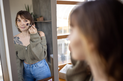 A young woman applying make-up to her face in the bathroom of her apartment