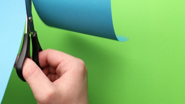 cutting blue paper with scissors on a green background