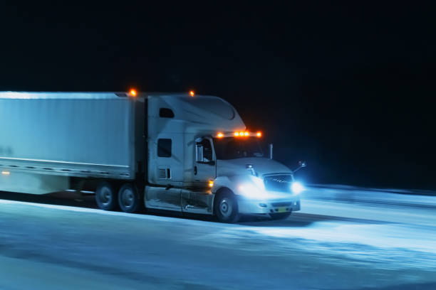 A semi truck drives on a snow covered highway at night.