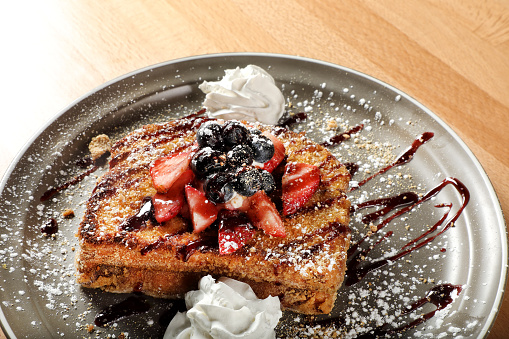 French toasts with strawberry and powdered sugar for breakfast on a wooden table