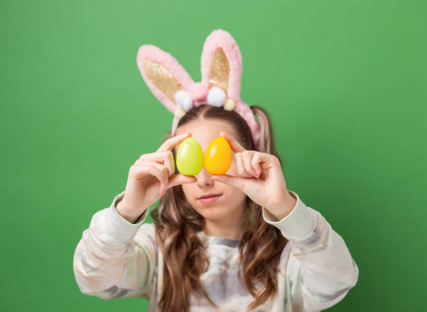 happy easter. funny cute girl with easter bunny ears and colorful easter eggs on green background. copy space. - easter easter bunny fun humor stock-fotos und bilder