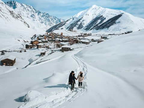 Couple walks looking at beautiful snow-capped mountain landscape in Georgia's Ushguli region.