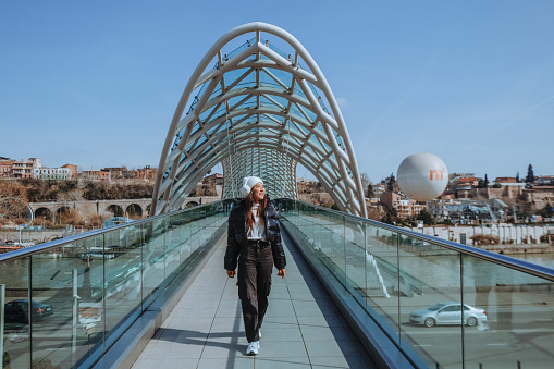 A young woman walks along the Bridge of Peace City center attractions Bridge over the beautiful river of Tbilisi in the state of Georgia.