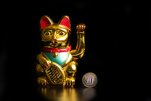 Symbolic figurine of a Chinese souvenir cat that brings financial luck and a coin of 10 Chinese yuan