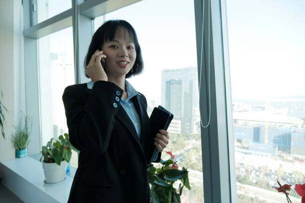 istock Asian woman happily discussing business using mobile phone at office window 1942504811