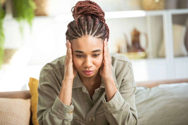 Worried young women sitting on sofa at home Sad teenage girl with braided hair sitting on sofa in her room, holding he’d in hands, looking down. head in hands stock pictures, royalty-free photos & images