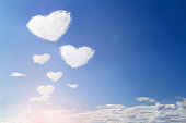 Fluffy clouds forming a hearts shape on blue sky, soft focus.