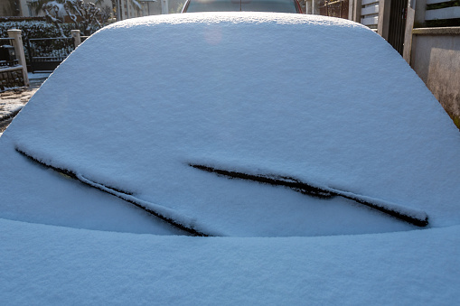 Close-up of the front of a car covered in a layer of snow on the street on a cold winter morning