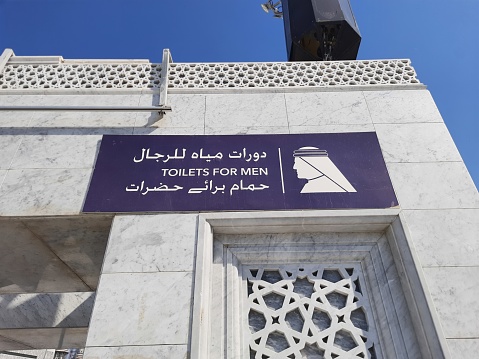 A blue sign written in Arabic, English and Urdu: Toilets for men in front of the Grand Mosque in Mecca, which is the holiest place for Muslims