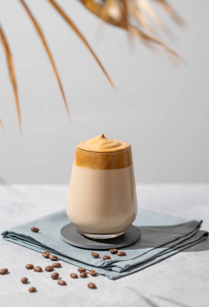 istock Dalgona coffee. Whipped instant coffee in a glass with beans and palm leaf shadow on a light background. 1942609073