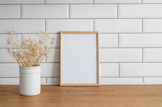 istock A light frame with a blank canvas against a white tile wall and on a wooden tabletop with dry bouquet. 1942610134