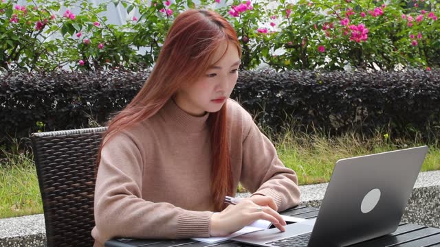 A young Chinese lady is doing an online business on her laptop in a sidewalk cafe