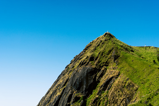 A towering mountain peak covered in lush greenery rises sharply against a clear blue sky.