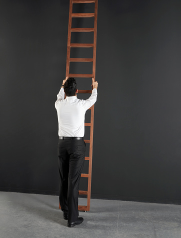 Businessman and ladder in front of a blackboard wall