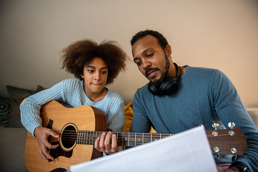 Father teaching his daughter playing guitar.