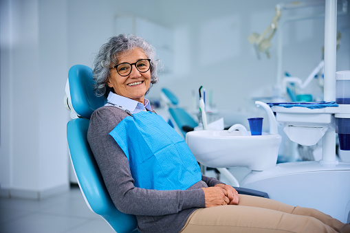Happy senior woman in dentist's chair looking at camera. Copy space.