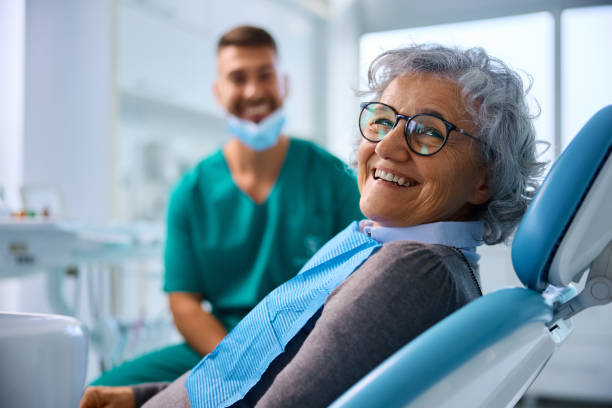 Satisfied senior woman at dentist's office looking at camera. Happy senior woman at dental clinic looking at camera. Her dentist is in the background. at the dentist stock pictures, royalty-free photos & images