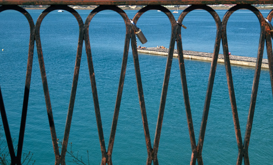 Looking through a wrought iron fence, sunbathers below on a wharf