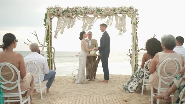 Mature marriage celebrant performing wedding ceremony on the beach