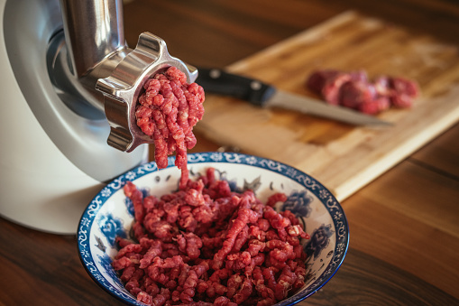 Electric meat grinder with mince in a bowl at a domestic kitchen