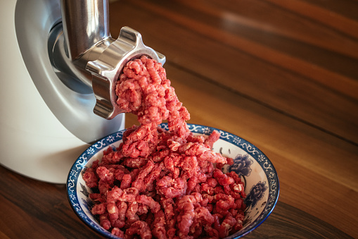 Electric meat grinder with mince in a bowl at a domestic kitchen