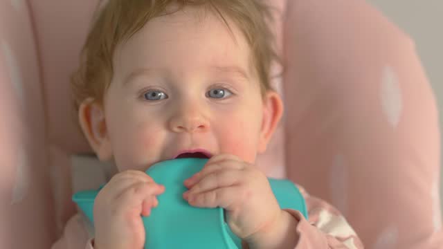 Baby with blue bib eating and playing in a high chair in 4k slow motion 60fps