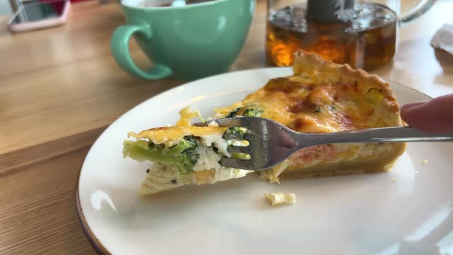 cut cheese tart with broccoli spinach and salmon with a fork in a cafe on a wooden table white plate next to tea with flowers Vasilkov delicious lunch snack lunch