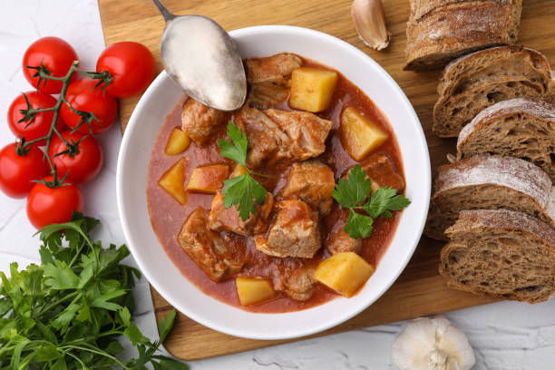 istock Delicious goulash in bowl, bread and ingredients on white textured table, flat lay 1942776530