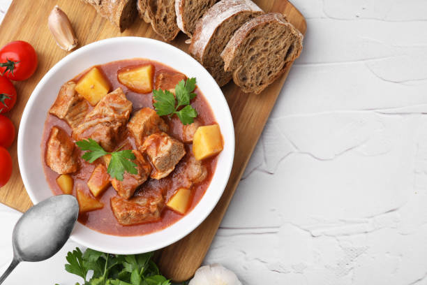 istock Delicious goulash in bowl and ingredients on white textured table, flat lay. Space for text 1942776532