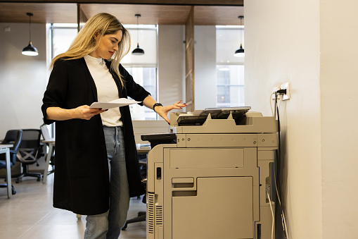 Attractive businesswoman in casual clothes making some copies in a photocopier at work