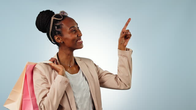 Black woman, shopping bag and pointing in advertising, sale or discount against a studio background. Portrait of happy African female person or shopper showing notification, alert or promo on mockup