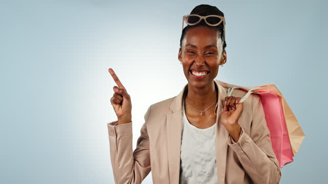 Happy black woman, shopping bag and pointing in advertising, sale or discount against a studio background. Portrait of African female person or shopper showing notification, alert or promo on mockup