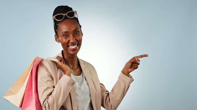 Black woman, shopping bags and pointing in advertising, sale or discount against a studio background. Portrait of happy African female person or shopper showing notification, alert or promo on mockup