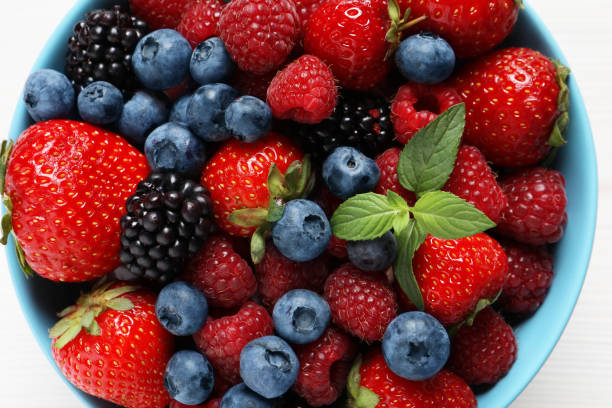 istock Many different fresh ripe berries in bowl on white wooden table, top view 1942803610