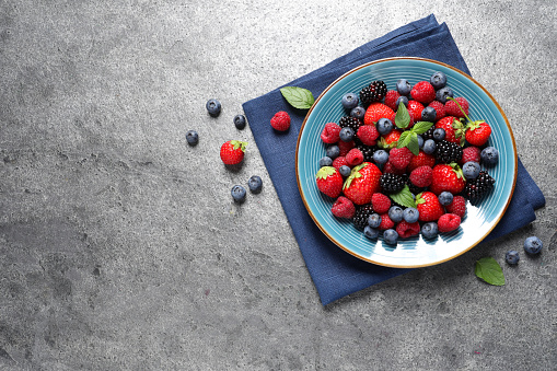 Many different fresh ripe berries in plate on grey table, flat lay. Space for text