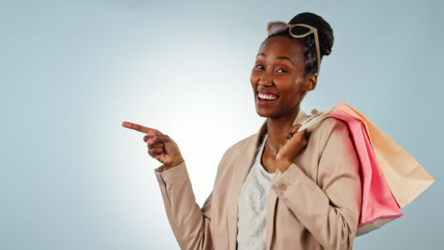 Happy black woman, shopping bags and pointing in advertising, sale or discount against a studio background. Portrait of African female person or shopper showing notification, alert or promo on mockup