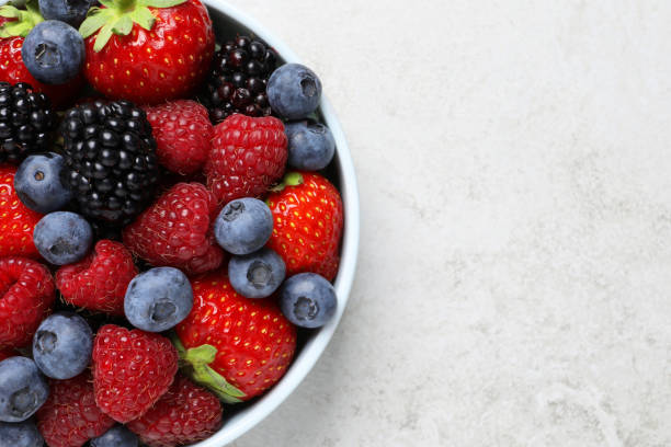 istock Many different fresh ripe berries in bowl on light grey table, top view. Space for text 1942804673