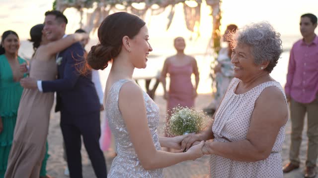 Bride talking and embracing grandmother after wedding ceremony on the beach