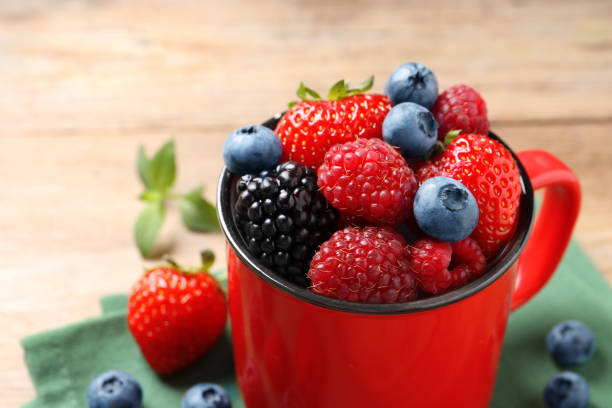 istock Many different fresh ripe berries in mug on wooden table, closeup. Space for text 1942804685
