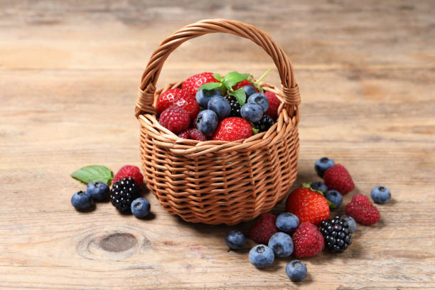 istock Wicker basket with many different fresh ripe berries on wooden table 1942805216