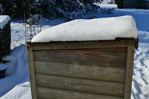 Pine wood garden equipment storage shed covered with a layer of fresh snow on a sunny morning